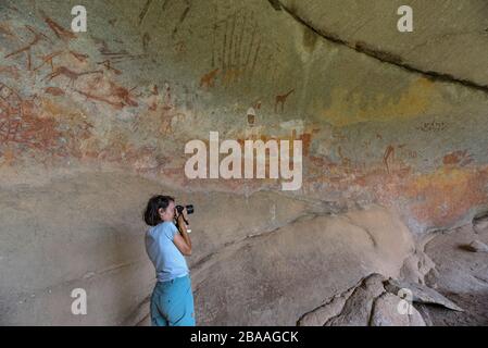 Un touriste prend une photo de l'art rupestre de San dans la grotte d'Inanke, le parc national de Matobo, au Zimbabwe. Banque D'Images