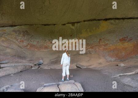 Un touriste admire l'art rupestre de San dans la grotte d'Inanke, parc national de Matobo, Zimbabwe. Banque D'Images