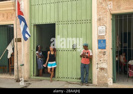 Homme cubain se tenant à l'extérieur du bureau et femme à l'intérieur du bureau tous deux regardant une jeune femme se tenant à l'entrée à la Havane Banque D'Images