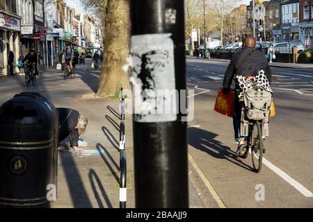 Londres, Royaume-Uni. 26 mars 2020. Verrouillage du coronavirus. Chiswick High Road pavé artiste et cyclistes. Un pavé artistes croches, craie à la main, sur une image que les cyclistes utilisent la route et le pavé. Crédit: Peter Hogan/Alay Live News Banque D'Images