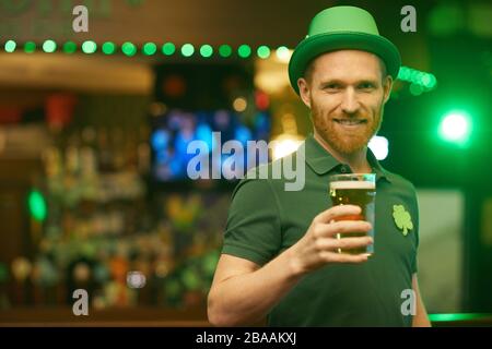 Portrait d'un jeune homme barbu portant un chapeau vert et tenant un verre de bière, il célèbre la Saint Patrick Banque D'Images
