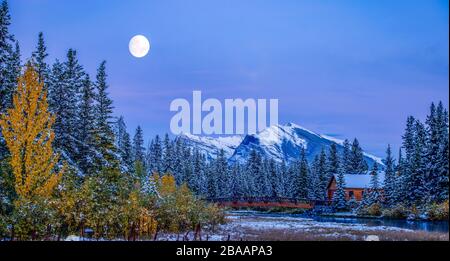 Moon over Pigeon Mountain et chalet en bois et pont près du ruisseau Policaemans, Canmore, Alberta, Canada Banque D'Images