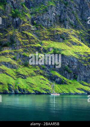 Paysage pittoresque avec un petit voilier solitaire sur fond de roches abruptes colorées. Norvège Banque D'Images