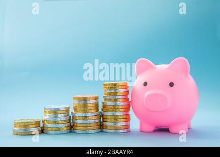Un concept d'épargne pour enfants de piles de pièces d'or et d'argent créant une prévision de bénéfice vers une banque piggy rose pour enfants avec espace de copie Banque D'Images