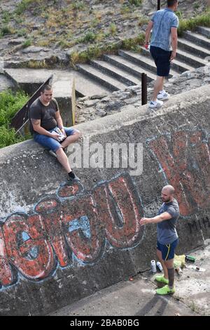 Sur un mur vertical en béton, trois jeunes hommes se tiennent et se préparent à imprimer des graffitis Banque D'Images