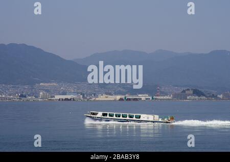 Ferry Aqua Net en direction du Parc commémoratif de la paix à Miyajima avec Hiroshima en arrière-plan, Hiroshima, Japon Banque D'Images