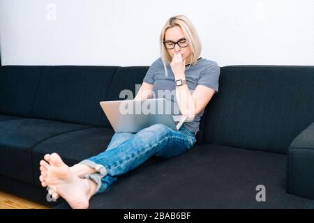 Formation et travail en ligne à distance. Une femme travaillant au bureau travaille à distance à domicile. Femme décontractée avec lunettes à l'aide d'un ordinateur portable à huis Banque D'Images