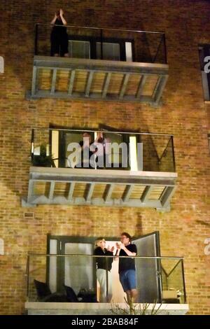 RETRANSMETTRE L'AJOUT de PERSONNES DE LIGNE DE CORRESPONDANCE à Wapping Wharf, Bristol, sortir sur leur balcon pour se joindre à un applaudissement national pour le NHS de leurs portes, fenêtres et balcons pour montrer leur appréciation pour tous les travailleurs du NHS qui aident à combattre le Coronavirus. Banque D'Images