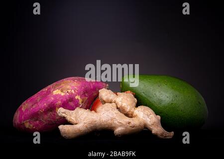 Le studio à faible clé reste la vie de divers légumes avec la patate douce, l'oignon, l'avocat et le gingembre en face avec un fond gris foncé Banque D'Images