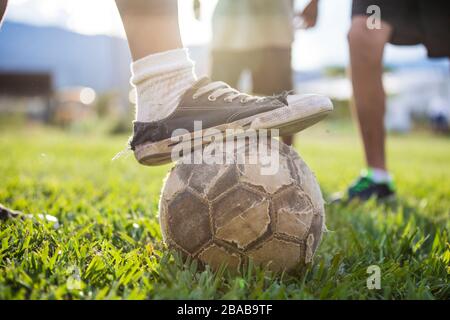 Le joueur de football (football) place la vieille chaussure sur un ballon de football déchiré. Banque D'Images