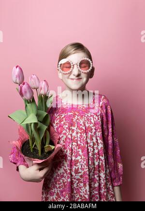 Mod, fille excentrique, peau équitable, portant des tulipes roses sur fond rose Banque D'Images