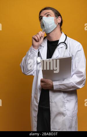 Le médecin portant un peignoir blanc, un stéthoscope et un masque tient une carte et un stylo près de sa bouche qui débouche sur le remède du virus du sras-cov-2 Banque D'Images