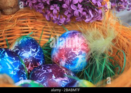 Fond de Pâques. Œufs décorés d'art avec du lilas et des plumes dans le panier. Motifs et couleurs artistiques sur les œufs. Banque D'Images