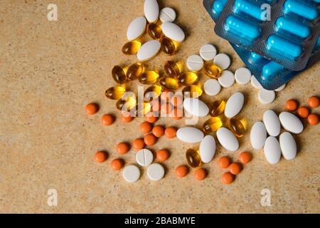 Les plaquettes thermoformées avec pilules bleues, roses et orange, les capsules de vitamine D et d'huile de poisson se trouvent au hasard sur les plans de travail sur fond de sable Banque D'Images