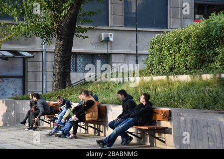 A côté du grand bâtiment se trouve un parc avec un immense arbre. Il y a trois bancs dans le parc où se trouve un groupe d'adolescents Banque D'Images