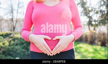 Blonde femme enceinte debout dehors sur un après-midi ensoleillé de printemps et tenant ses mains sur son ventre Banque D'Images