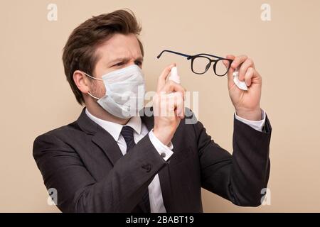 Homme caucasien dans un masque médical portant un costume désinfectant les lunettes. Précaution contre le coronavirus ou toute autre infection. Banque D'Images