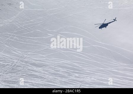 Ombre de l'hélicoptère sur la piste de ski enneigée hors piste avec traces de skis et de snowboards à la journée ensoleillée d'hiver. Heli-ski dans les hautes montagnes. Banque D'Images