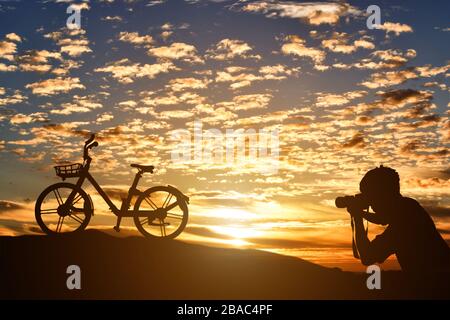 Silhouette du photographe prenant des photos d'un vélo au coucher du soleil fond. Banque D'Images
