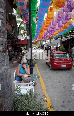 Détente touristique et lecture sous les bannières papel picado dans le centre de Sayulita, au Mexique. Banque D'Images