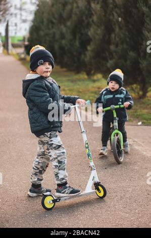 POZNAN, POLOGNE - 21 mars 2020: Jeune garçon qui monte un scooter sur une piste d'asphalte avec garçon assis sur un vélo de course dans un fond doux. Banque D'Images