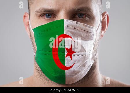 Jeune homme aux yeux douloureux dans un masque médical peint dans les couleurs du drapeau national de l'Algérie. Protection médicale contre les maladies aéroportées, corona Banque D'Images