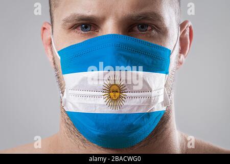 Jeune homme aux yeux douloureux dans un masque médical peint dans les couleurs du drapeau national de l'Argentine. Protection médicale contre les maladies aéroportées, coro Banque D'Images