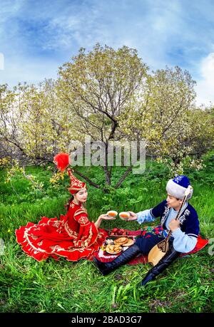 Couple en costume Kazakh assis au printemps fleurs jardin apple au picnic à Almaty, Kazakhstan, en Asie centrale Banque D'Images