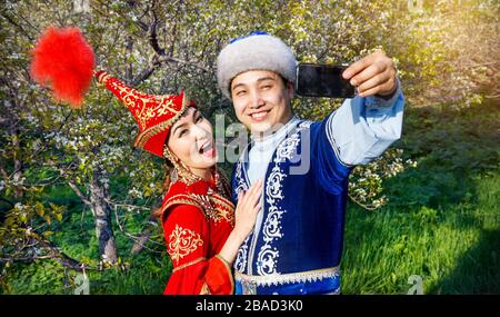 Portrait of Happy couple en costumes Kazakh faisant par téléphone portable selfies en fleurs de printemps dans le jardin d'apple d'Almaty, Kazakhstan, en Asie centrale Banque D'Images