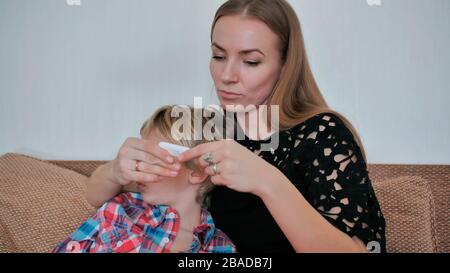 Une mère bienveillante mesure la température de son fils avec un thermomètre. Banque D'Images