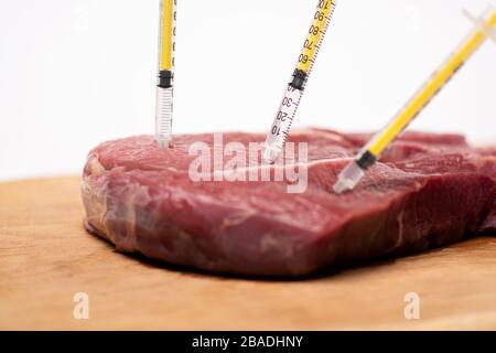 Focalisation sélective des seringues dans la viande brute sur le tableau de découpe isolé sur blanc Banque D'Images