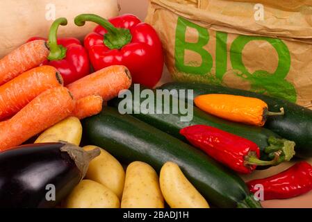 Légumes biologiques présentés sur une planche à découper en bois. En arrière-plan, un sac en papier écologique avec le mot « BIO » imprimé en vert. Banque D'Images