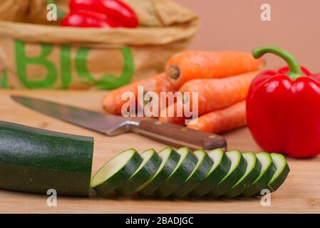 Légumes biologiques présentés sur une planche à découper en bois. En arrière-plan, un sac en papier écologique avec le mot « BIO » imprimé en vert. Banque D'Images