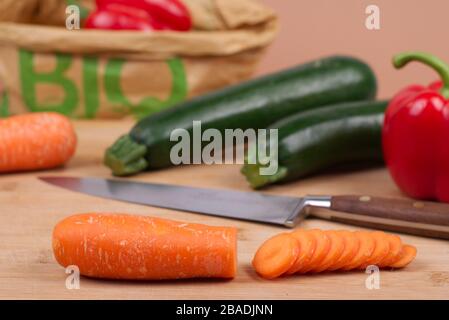 Légumes biologiques présentés sur une planche à découper en bois. En arrière-plan, un sac en papier écologique avec le mot « BIO » imprimé en vert. Banque D'Images