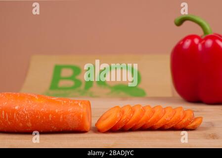 Légumes biologiques présentés sur une planche à découper en bois. À l'arrière-plan, un sac en papier avec le mot « BIO » imprimé en vert. Banque D'Images