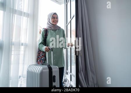 une jeune femme voilée ouvrit la porte avec son sac et sa valise après un long séjour Banque D'Images