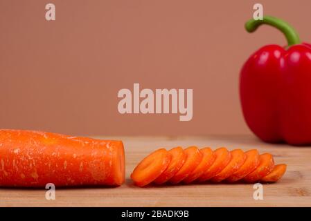 Une carotte biologique et un poivron rouge présentés sur une planche à découper en bois. La carotte orange est coupée en tranches. Représente un mode de vie sain et biologique. Banque D'Images