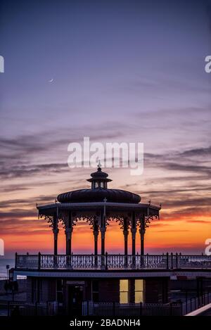Brighton, Royaume-Uni, le 26 mars 2020, le soleil se couche derrière le kiosque à bande sur le front de mer de Hove ce soir alors que le pays s'isole contre le coronavirus. Banque D'Images