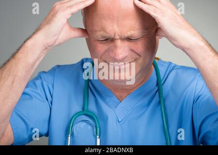 Médecin affolé avec ses mains sur sa tête, portant des gommages bleus avec stéthoscope, contre un fond clair. Banque D'Images