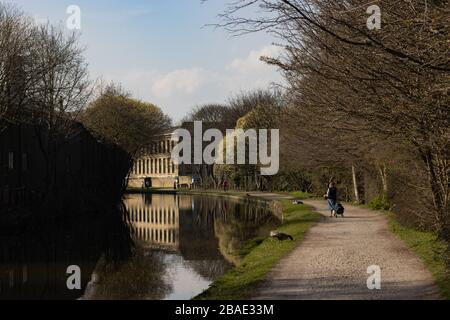 SALTAIRE, ANGLETERRE - 25/3/2020 - une dame âgée solitaire marche le long du canal de Shipley vers New Mill vu à l'horizon avec un sac de shopping Banque D'Images