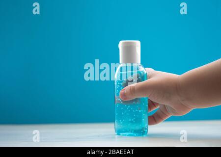 Main de l'enfant tenant une bouteille de gel désinfectant pour les mains. L'hygiène des mains comme protection contre le coronavirus. Produit antivirus et antibactérien. Liquide bleu avec granulés ronds blancs. Copier l'espace pour le texte Banque D'Images