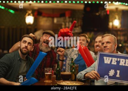 Un groupe de fans de football assis à la table et applaudisse pour leur équipe préférée au bar sportif Banque D'Images