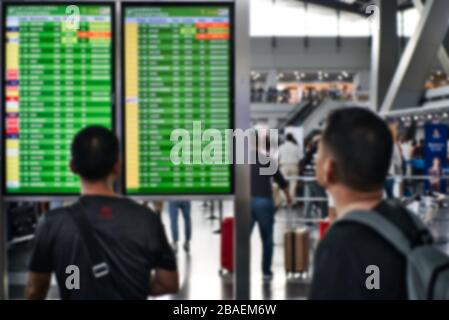 Photo floue des passagers regardant le panneau des vols d'un aéroport pour confirmer l'état de leurs vols. Banque D'Images