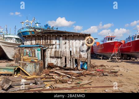 Un petit bâtiment en bois de merde parmi beaucoup de panneaux, et de vieux navires rouillés en réparation situés sur un quai sec grungy dans le chantier naval contre le ciel bleu le jour ensoleillé dans l'ancienne usine de construction navale Banque D'Images