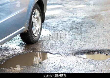 Gros plan sur la roue d'une route en très mauvais état avec de grandes cahules pleines de piscines d'eau de pluie sale. Banque D'Images