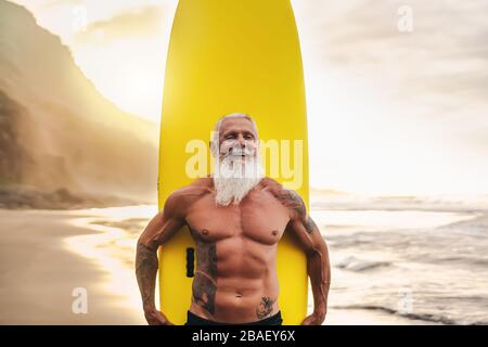 Bonne tenue pour les personnes âgées qui s'amusent à surfer au coucher du soleil - Sporty barbu homme s'entraîner avec planche de surf sur la plage Banque D'Images