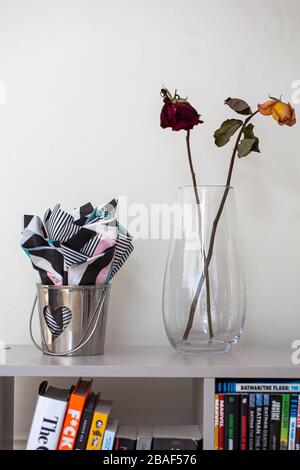 Un vase avec quelques roses séchées à côté d'un seau d'argent avec une forme de coeur découpée. À l'intérieur se trouvent de belles serviettes. Banque D'Images