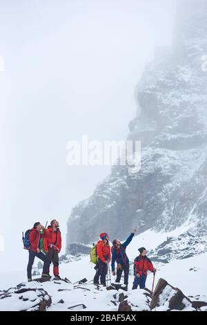 Alpinistes mâles debout sur une colline rocheuse et regardant la haute montagne couverte de neige. Randonneurs avec sacs à dos discutant comment atteindre le sommet de montagne. Concept d'alpinisme, de randonnée et d'alpinisme. Banque D'Images