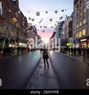 Oxford Street, Londres. Vue sur le quartier commerçant animé de Londres avec un acheteur anonyme admirant les lumières de Noël et le coucher du soleil. Banque D'Images