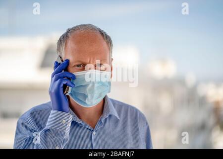 Un homme utilisant des masques de protection et des gants en latex bleu lors de l'utilisation du téléphone mobile dans les paysages urbains Banque D'Images